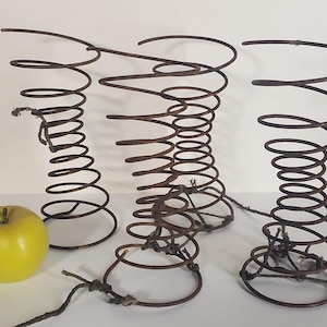 May include: Three rusty metal bed spring bases, each with a circular top and a spiral design. The springs are tied together with twine.