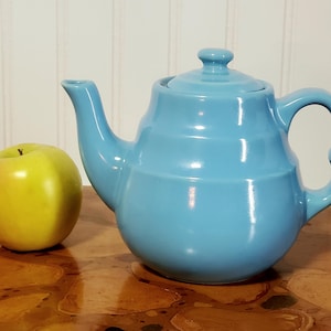 May include: A set of three ceramic mugs with a speckled, cream-colored glaze. Each mug features a different hand-painted floral design in shades of blue, green, and yellow. The mugs have a simple, rounded shape and a comfortable handle.