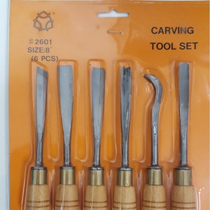 May include: A set of six carving tools with wooden handles. The tools are packaged in a clear plastic blister pack on a bright orange background. The package says "# 2601 SIZE: 8" (6 PCS) CARVING TOOL SET".