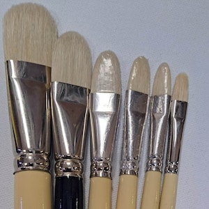 Może przedstawiać: Zestaw sześciu pędzli malarskich z drewnianymi uchwytami i srebrnymi obręczami. Pędzle są oznaczone rozmiarem i nazwą marki "SOC. INT. CAN. TOBGI MTL. 3212 Niemcy".