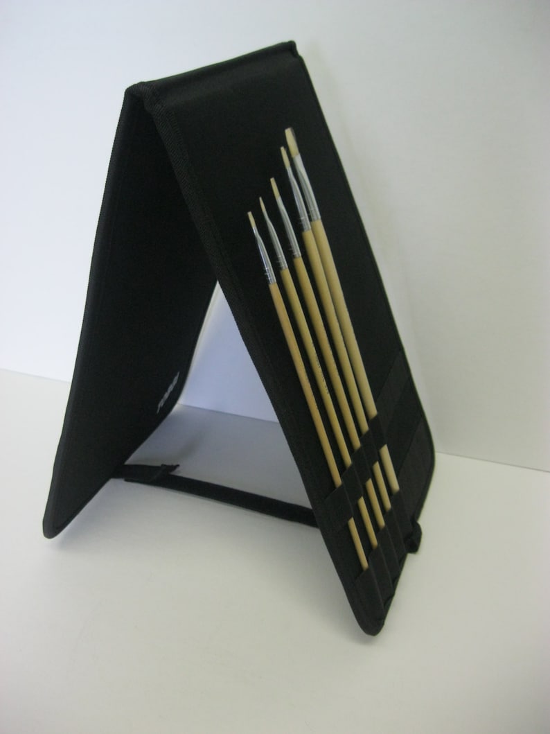 May include: A black, foldable brush holder with six paintbrushes inside. The brushes are made of wood and have different sizes.