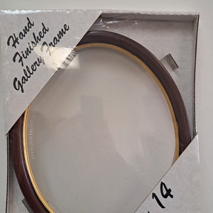 May include: An oval picture frame with a brown and gold finish and a clear glass insert. The frame is labelled "Hand Finished Gallery Frame" and "11 x 14".
