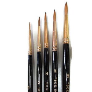 May include: Set of five paint brushes with black handles and gold lettering. The brushes are labelled "0", "1", "3", "4", and "5" and are arranged from smallest to largest.