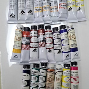 Peut inclure: Une collection de 18 tubes de peinture &agrave; l'huile Van Dyck, dispos&eacute;s en trois rang&eacute;es. Les tubes sont &eacute;tiquet&eacute;s avec le nom de la couleur, le num&eacute;ro et la marque. Les couleurs comprennent le blanc, le jaune, le rouge, l'orange, le brun, le bleu, le vert et le noir.