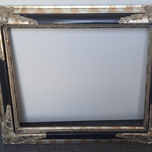 Può includere: Una cornice per foto ornata in nero e argento con un design decorativo. La cornice ha un bordo largo e un bordo rialzato.