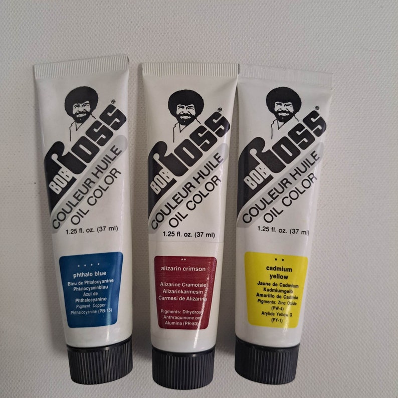 May include: Three tubes of Bob Ross brand oil paint. The tubes are labeled with the colors phthalo blue, alizarin crimson, and cadmium yellow. Each tube is 1.25 fluid ounces (37 ml).