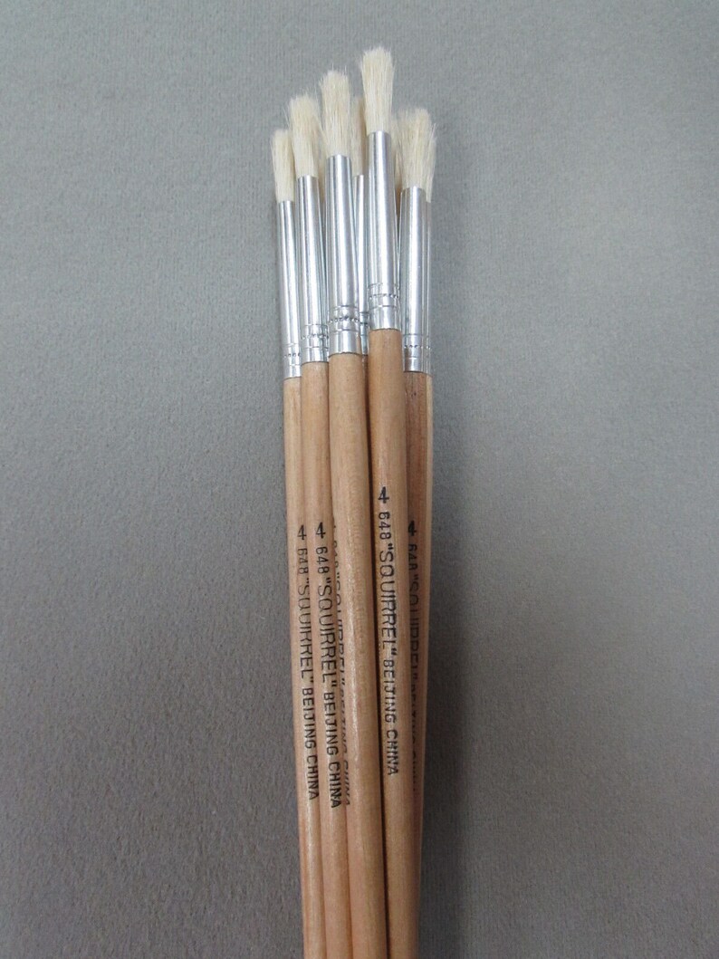 May include: A bundle of six paint brushes with wooden handles and silver ferrules. The brushes have white bristles and are labeled "648 "SQUIRREL" BEIJING CHINA".