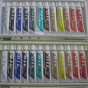 May include: Two open boxes of oil paint tubes. Each tube is labeled with the word "OIL" and the color name. The tubes are arranged in rows, with a variety of colors including black, blue, green, yellow, brown, and red.