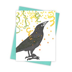 May include: A black crow with a yellow and green confetti design around it. The crow is looking up at the confetti.