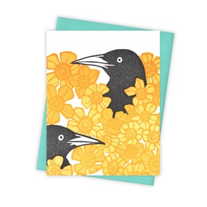 May include: Two black birds with yellow eyes are partially hidden in a cluster of yellow flowers. The birds are facing opposite directions. The background is white.