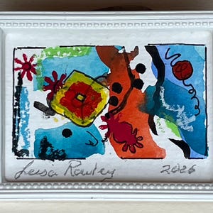 May include: A small rectangular white frame containing an abstract watercolor painting with vibrant patches of blue, orange, yellow, and green. The artwork features hand-drawn black ink shapes, including stars and dots, with the signature Leisa Rowley and 2026.