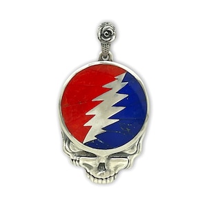 May include: A silver pendant featuring a skull design with a red, white, and blue emblem. The emblem has a lightning bolt design. The pendant has a rose detail at the top.