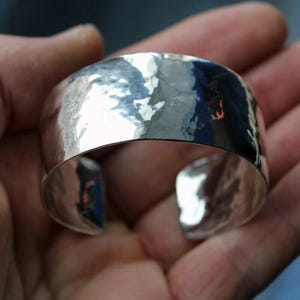 May include: A silver hammered cuff bracelet. The bracelet is wide and has a smooth, polished finish.