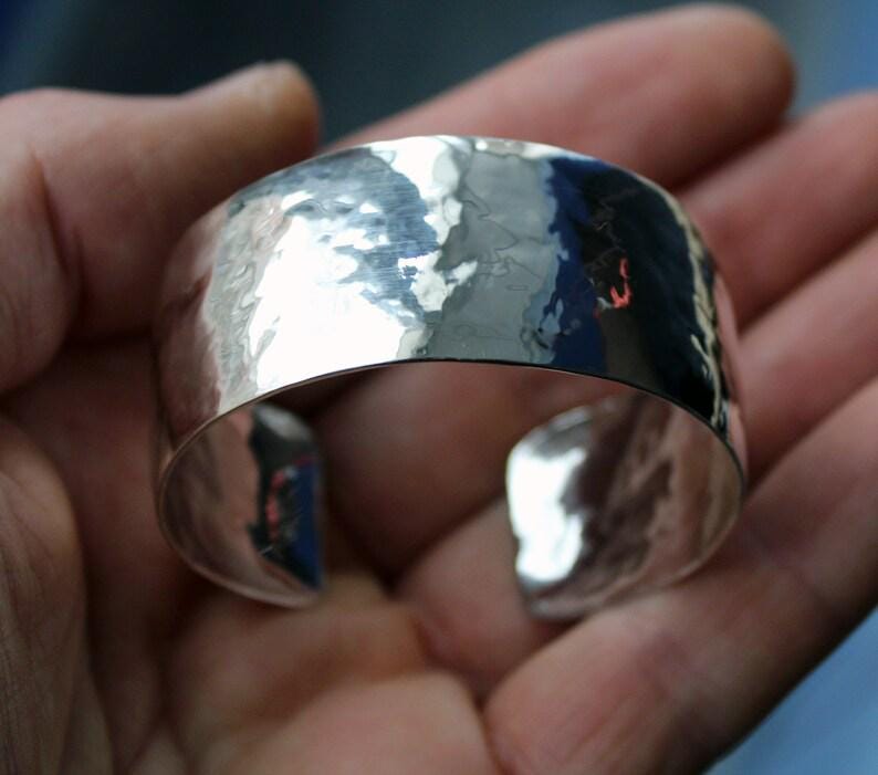 May include: A silver hammered cuff bracelet. The bracelet is wide and has a smooth, polished finish.