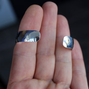 May include: Two silver hammered metal rings, one on each finger, worn on a person's hand.