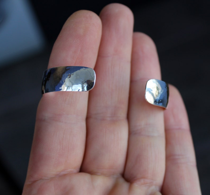 May include: Two silver hammered metal rings, one on each finger, worn on a person's hand.