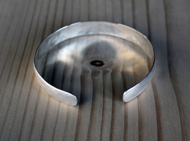 May include: A silver bangle bracelet with a brushed finish.