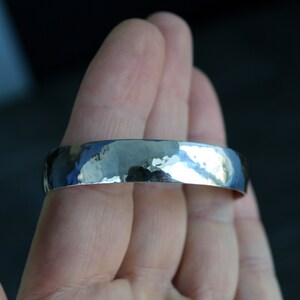 May include: A silver hammered bangle bracelet. The bracelet is smooth and shiny, with a slightly rounded shape.