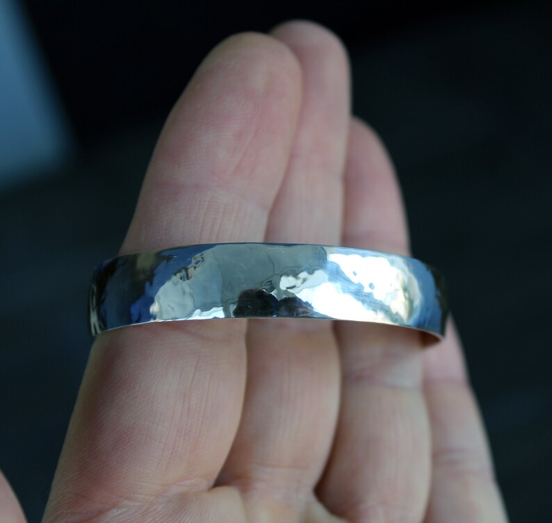 May include: A silver hammered bangle bracelet. The bracelet is smooth and shiny, with a slightly rounded shape.