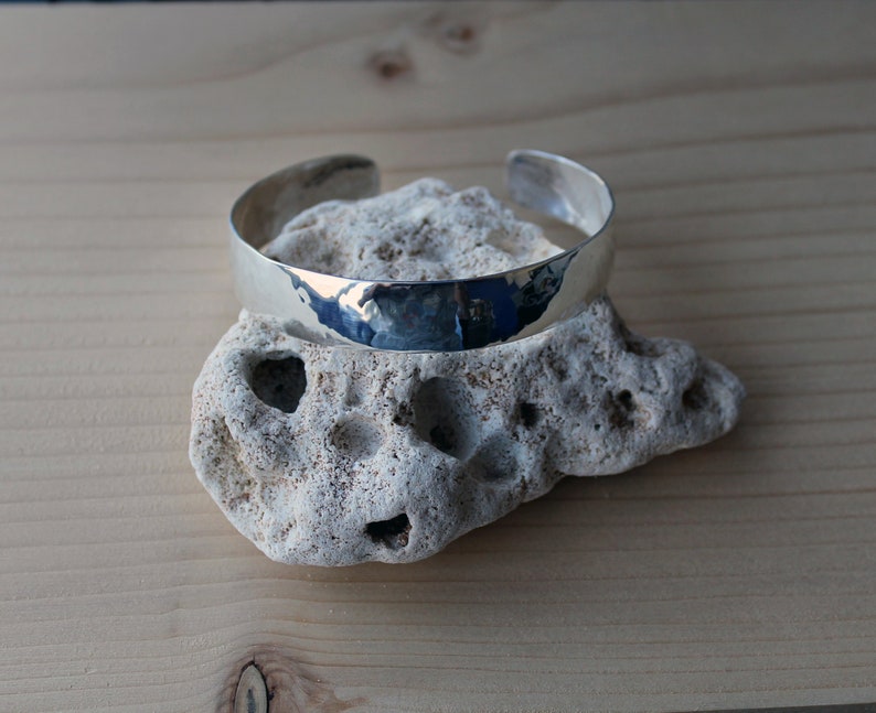 May include: A silver hammered bangle bracelet, resting on a white rock.