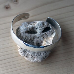 May include: A silver hammered bangle bracelet, resting on a piece of rough, white coral.
