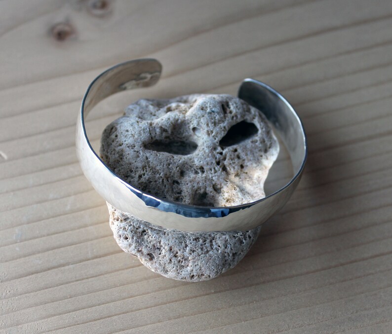 May include: A silver hammered bangle bracelet, resting on a piece of rough, white coral.