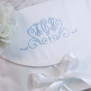 May include: White baby blanket with a blue embroidered monogram and a white satin ribbon tied in a bow.