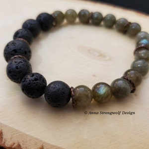 May include: A beaded bracelet featuring black lava rock beads and iridescent labradorite beads. The bracelet is strung with copper-colored accents. The bracelet is displayed on a light wood surface.