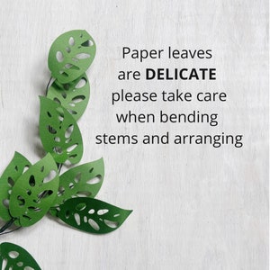 K&ouml;nnte beinhalten: Gr&uuml;ne Papierbl&auml;tter mit ausgeschnittenen Designs, die in einem kaskadierenden Muster angeordnet sind. Der Text lautet: "Papierbl&auml;tter sind DELIKAT, bitte gehen Sie beim Biegen der Stiele und beim Anordnen vorsichtig vor."