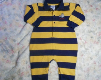 May include: A long-sleeve romper featuring horizontal navy blue and yellow stripes, a navy blue polo collar, and a button-up placket. An embroidered graphic of a seal with the text OshKosh is positioned on the upper left chest area.