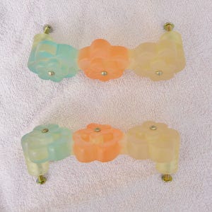 May include: Two sets of floral cabinet pulls. Each pull features three flower-shaped elements in shades of blue, orange, and yellow. The pulls are attached with gold-colored screws, and are likely made of resin or a similar material.