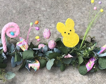 May include: A green garland with pink and yellow candy decorations, including a yellow bunny, for Easter.