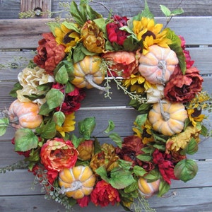 May include: A fall-themed wreath featuring orange, red, and yellow flowers, green leaves, and small, pale yellow pumpkins.