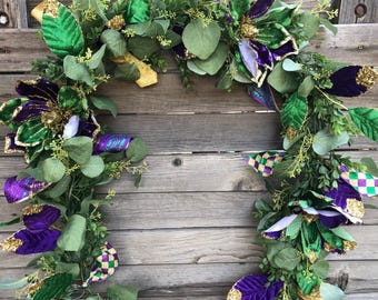 May include: A Mardi Gras garland with green, purple, and gold accents. The garland features velvet flowers, green leaves, and gold glitter.