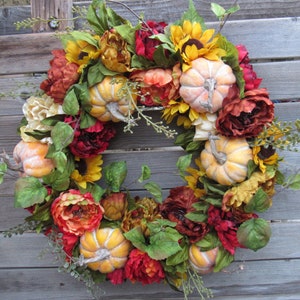 May include: A fall-themed wreath with red, orange, and yellow flowers, green leaves, and small pumpkins.