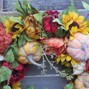 May include: A fall-themed wreath featuring sunflowers, peonies, and pumpkins. The wreath is decorated with greenery and has a rustic feel.
