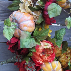 May include: A fall-themed wreath featuring orange and yellow pumpkins, red and orange peonies, and green leaves.