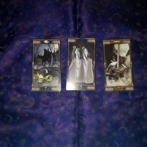 May include: Three tarot cards with ornate gold frames. The first card shows a figure on horseback riding through a dark forest. The second card shows three figures in white robes holding chalices. The third card shows a figure holding a sword.