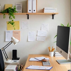 May include: A home office workspace with a wooden desk, a computer monitor, a lamp, and a shelf with folders and books. Papers are pinned to the wall behind the desk.