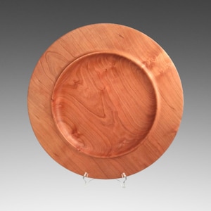 May include: A round wooden serving platter made of cherry wood. The platter has a raised edge and a smooth, polished finish.