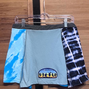 May include: A blue and black tie-dye skirt with a patch of a band of dancing figures. The skirt has a gray waistband.