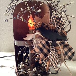 May include: A rustic metal candle lantern with a black crow silhouette, decorated with white and black checkered fabric, and white berry sprigs.