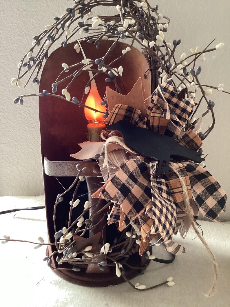 May include: A rustic metal candle lantern with a black crow silhouette, decorated with white and black checkered fabric, and white berry sprigs.