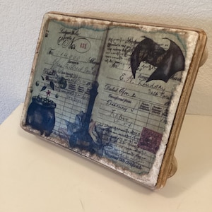 May include: A wooden box with a vintage ledger design featuring a bat, a cauldron, and handwritten text. The text includes "Ledger No. 451", "14,000 Shares", "Chase, Streck & Tone", "Issued", "& A. Ludsary", "Dated Apr. 1", "Transferred from Treasury", "Raber", and "Salt Pans".