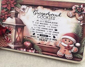 Könnte beinhalten: Ein Holzschild mit einem Lebkuchenmann und einer Laterne, mit einem Rezept für Lebkuchen. Das Rezept enthält Zutaten wie braunen Zucker, Melasse, Butter, Mehl, Natron, Zimt, Ingwer, Muskatnuss und Nelken. Das Schild sagt auch "Backen bei 375° für 10 Minuten - Guten Appetit".