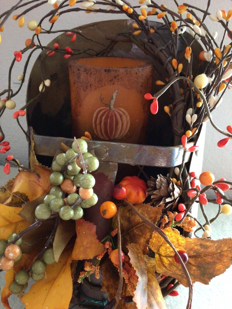May include: A rustic metal scoop with a fall-themed arrangement. The scoop holds a brown candle with a pumpkin design. The arrangement includes fall leaves, berries, and twigs.