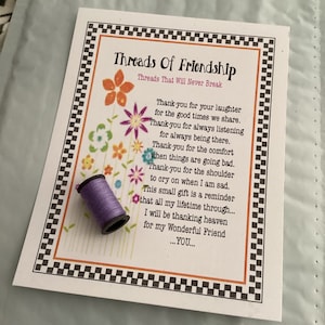 May include: A purple spool of thread with a white card that reads "Threads of Friendship" with a poem about friendship. The card has a black and white checkered border.
