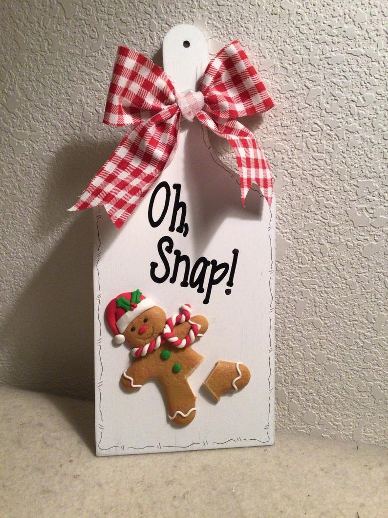 May include: White wooden sign with a red and white gingham bow. The sign says "Oh, Snap!" and features a gingerbread man with a broken leg.