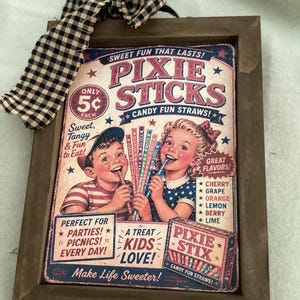 May include: A framed vintage-style sign featuring the text "Pixie Sticks Candy Fun Straws!" with illustrations of children enjoying the candy. The sign is in a brown wooden frame and has a black and white checkered bow at the top.