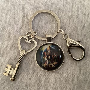 May include: A silver key chain with a heart-shaped key, a round charm with the text "Ancient Aliens" and a silver lobster clasp.
